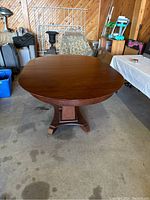 Photo showing oval mahogany dining table with double pedestal base in garage setting.