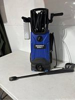 Front view of Simoniz electric pressure washer with hose rolled on top, spray gun on side, and detergent bottle attached.