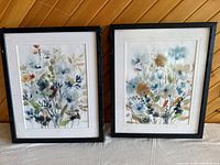 Pair of floral art prints in distressed black frames, showing scratches and wear, with paper backing damaged.