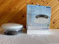 Flushmount ceiling light fixture in original packaging next to the boxed product, showing the bronze base and opaque glass shade.