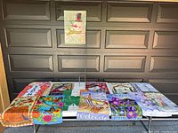 All 14 garden flags laid out on a flat surface with the metal flag stand centered behind them, showing various seasonal and holiday designs.