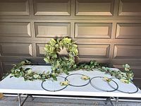 Photo showing the 8-foot lighted garland with green leaves, the green wreath, and four metal wreath forms on a table.