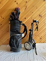 Photo of the golf clubs set inside black golf bag with multiple compartments and the foldable golf cart standing beside it.