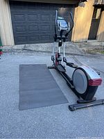 Photo of HealthRider elliptical and matching large black exercise floor mat on pavement outside garage.