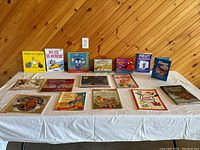 Display of 14 English and French books plus 2 boxed kits arranged on a table against a wooden wall.