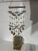 Full view of nautical wind chimes made of driftwood, sea glass, and seashells hanging above a sisal lantern containing a turquoise candle.