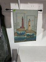 Full view of the nautical tapestry hanging on wall showing twin lighthouse panels and sailboats beneath, with hanging rod fixed through top edge