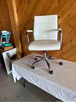 White leather office chair with chrome arms and caster wheels, positioned on a table with wooden paneled wall background.