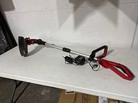 Full side view of Craftsman cordless rechargeable trimmer with battery and charger lying on table.