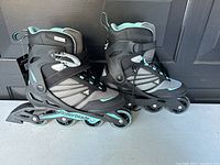 Side view of the pair of black and turquoise inline skates showing wheels and ankle support system