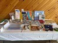 Full view of the scrapbooking lot on a table against a wooden wall showing various crafting tools, albums, and accessories arranged with cutting tools on the right and sticker sheets and templates in the center and left.