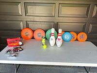 Photo showing three large frisbees, four smaller frisbees, two vintage bowling pins, golf balls, tees, and tennis balls on a folding table.