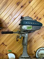 Side view of Evinrude outboard motor showing tiller handle and clamp mount against wooden wall