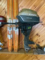 Front and side view of Scott-Atwater 16hp outboard motor mounted on a wooden wall with vintage waterskis beside it.