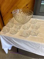 Photo of the entire punch bowl set displayed on a white tablecloth showing one large punch bowl and eleven matching cups arranged around it. The set features a raised bubble texture design on all pieces.