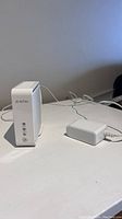 White AirTies WiFi extender device standing on table with power adapter plugged in and cable extending behind.