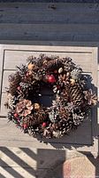 Pinecone decorated fall wreath featuring large and small pinecones, red berries, and other natural elements.