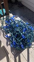 Photo of tangled string of blue Christmas lights with green wire on outdoor surface.