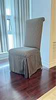 Front and side view of an upholstered dining chair with black and white vertical stripes, high back, and floor length skirt covering the legs.