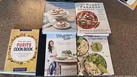 Top view of all five cookbooks laid out flat on a counter, showing front covers and partial titles clearly.