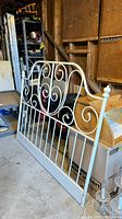 White metal headboard with scrollwork and vertical bars on a concrete floor in a workshop setting.