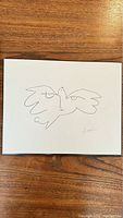 Photo of the print showing two doves drawn with simple continuous lines on white board with a small signature on bottom right.