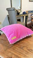 Solid bright pink velvet pillow with piping on table in room with striped chair and mirror.