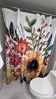 Photo showing the shower curtain hanging on a shower rod next to a toilet, displaying a floral motif.