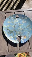 Ceramic painter's palette plate with printed 'Almond Blossom' artwork and 'Van Gogh Exhibited' text, placed on wooden surface.