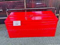 Closed red metal toolbox with black handle and latch