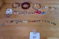 Full display of all jewelry items including bangles, rings, and various earrings arranged on wooden surface with lot tag number 41 visible.