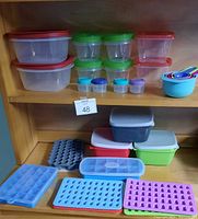 Photo showing various kitchen storage containers, condiment cups, color-coded measuring cups, and silicone ice cube trays arranged on wooden shelves.