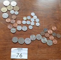 Coins and tokens spread out on wooden surface showing variety of copper, silver, and bi-metallic pieces including pennies, state quarters, and commemorative tokens.