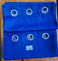 Two navy blue blackout curtain panels folded, showing 6 silver metal grommets on each panel lined up horizontally.