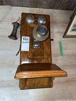 Front view of oak wall phone showing backboard, dual metal ringer bells, mouthpiece and separate earpiece lying to the side