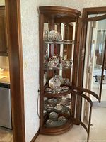 Wide shot of curved wooden display cabinet with shelves holding the porcelain Asian dinnerware set including plates, cups, saucers, teapot, cream, and sugar items.