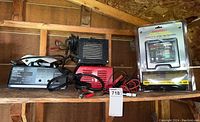 Three battery chargers on wooden shed shelf: Motomaster Powerfirst, black Eliminator Intelligent Battery Charger, and sealed 24V BatteryMINDer package