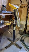Photo showing custom metal dust collector nozzle attached to a black adjustable metal pedestal stand with a yellow tip nozzle in a workshop setting.