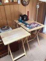 Overall view of 3 wooden folding tables with various flashlights and Makita batteries on top.