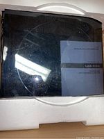 Top view of the turntable inside original styrofoam packaging with user manual visible under clear dust cover.