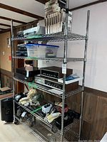 Full view of chrome metal shelving unit with items on shelves to demonstrate size and structure. Shows unit in a room against the wall.