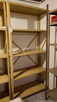 Full view of the metal shelf showing five flat shelves and structural frame with cross bracing, painted yellow, placed against wall in basement.