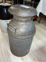 Full view of metal milk can with lid on, showing cylindrical shape and metal handles.