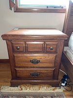 Front view of the wooden night side table showing three drawers with metal handles and knobs, and signs of wear on top surface.