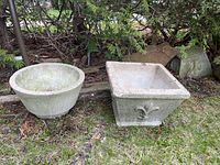 Wide view showing both concrete planters on ground near bushes outdoors