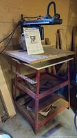 Radial arm saw on tool stand with manual attached, showing full setup and basement background.