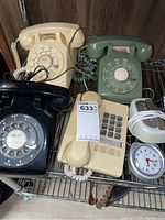 Overview of all items showing three rotary phones, one touch tone phone, and two alarm clocks on a metal shelf.