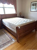 Three-quarter view of oak wood sleigh bed frame with mattress and box spring