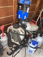 Image showing multiple sprayers including a 15L white and black backpack sprayer with straps, pump sprayers, and the boxed Power Fist spot sprayer on top.