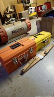 Photo showing two resin toolboxes, orange Deluxe Tuff and yellow toolbox, sitting on the floor with a RIDGID heater in the background